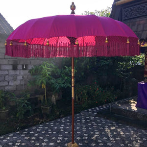 Balinese pink decorative umbrella with gold accents and fringe, outdoor garden setting