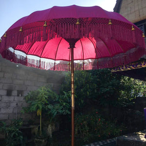 Large pink Balinese ceremonial umbrella with gold accents in a tropical garden setting