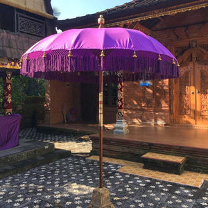 Purple Balinese umbrella with gold accents in front of hand-carved wooden entrance