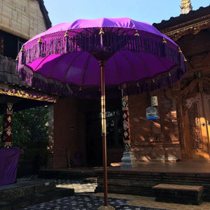 Purple Balinese parasol with fringe in front of carved wooden door and traditional architecture