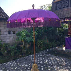 Purple Balinese parasol with fringe and gold accents in a garden courtyard