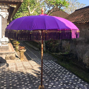 Purple Balinese decorative parasol with tassels in a traditional stone courtyard