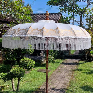 Balinese white decorative umbrella with gold accents and fringe, outdoor garden setting