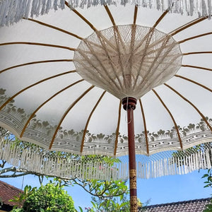 Balinese hand-carved garden umbrella with white fringe and gold pattern outdoors