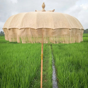 Handmade Balinese bamboo and jute umbrella with fringe in a lush green rice field