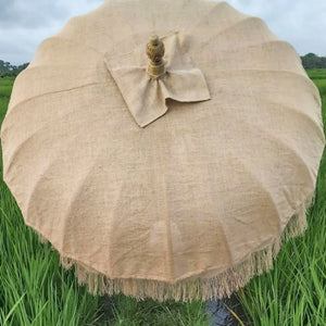 Handmade natural linen Balinese umbrella with tassels in a green rice field