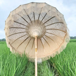 Handmade Balinese parasol with fringe detail in green rice field under cloudy sky