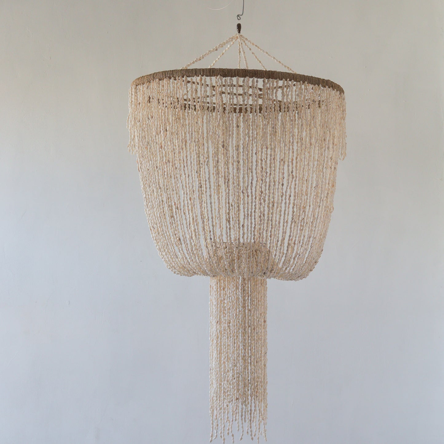 A beige seashell chandelier with a jelly fish design hanging against a neutral background.