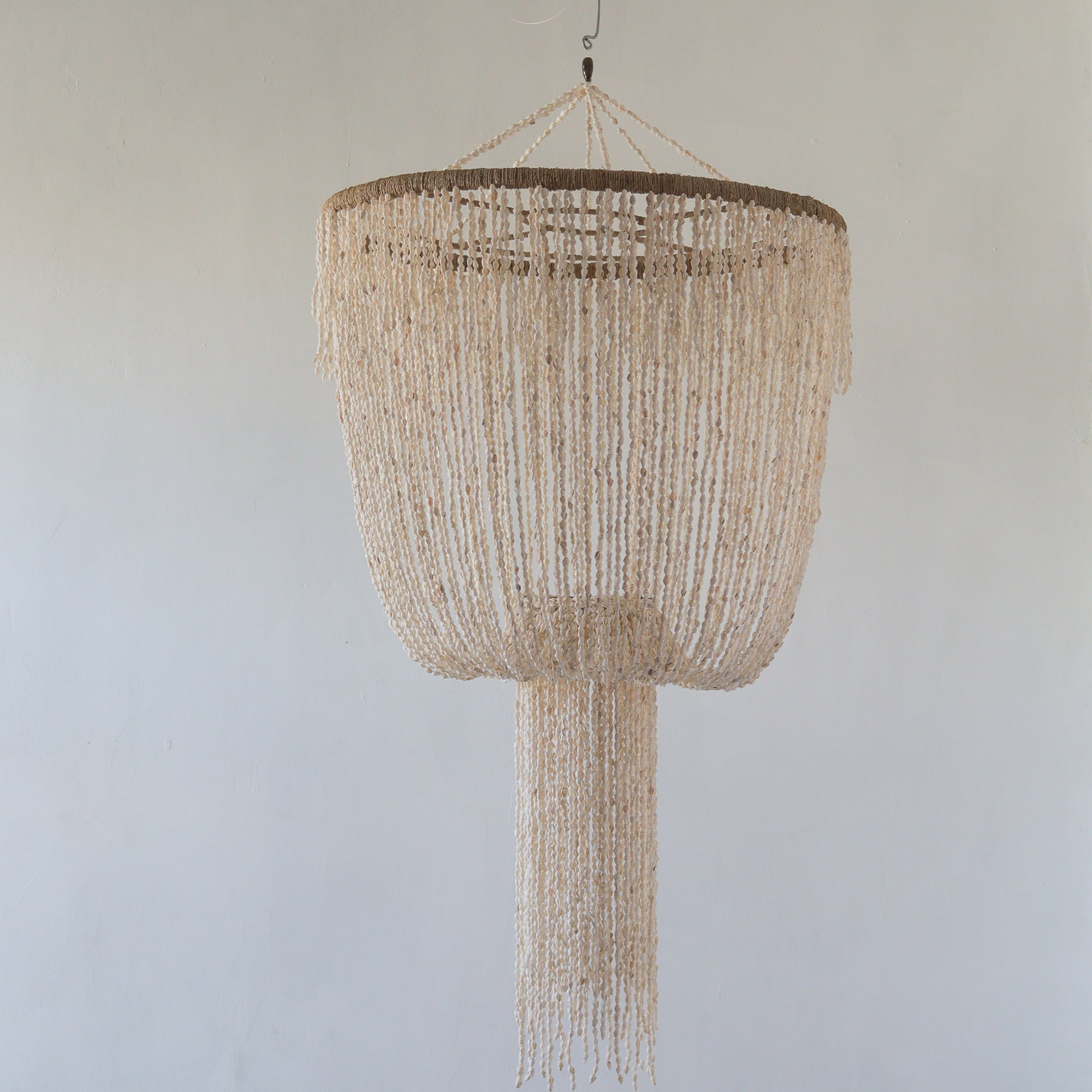A beige seashell chandelier with a jelly fish design hanging against a neutral background.