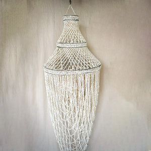 Handmade Balinese seashell chandelier with tiered design hanging against beige wall