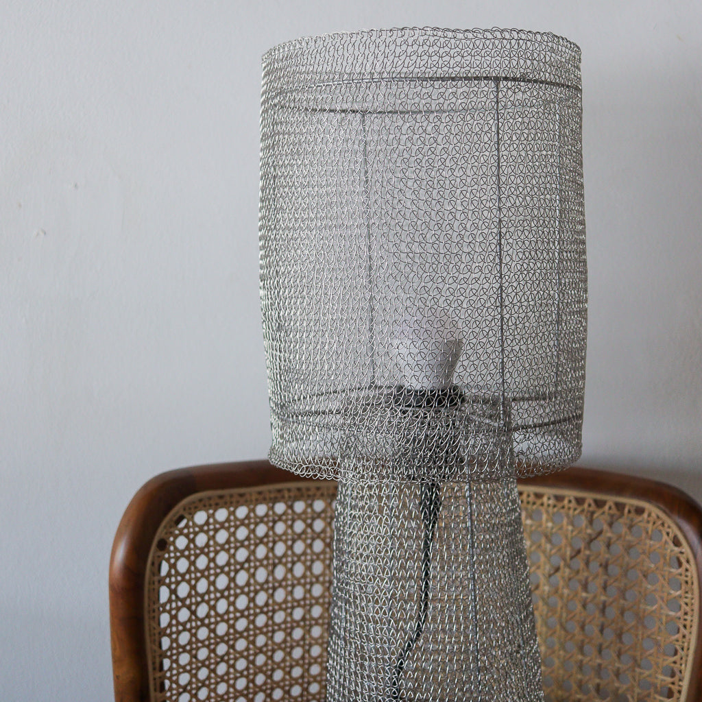 Metal wire mesh lampshade on a wooden chair against a plain background