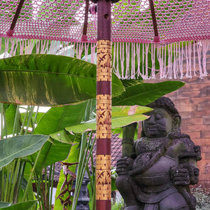 Balinese teakwood parasol with carved pole, purple canopy, garden statue, and tropical plants