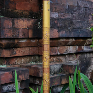 Hand-carved teakwood parasol pole with intricate patterns against brick wall outdoors