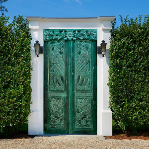 Green hand-carved Balinese vintage door gate with intricate patterns in outdoor garden.