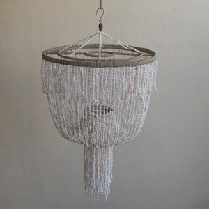 Handmade white seashell ceiling light with layered beaded strands, hanging against a plain wall.