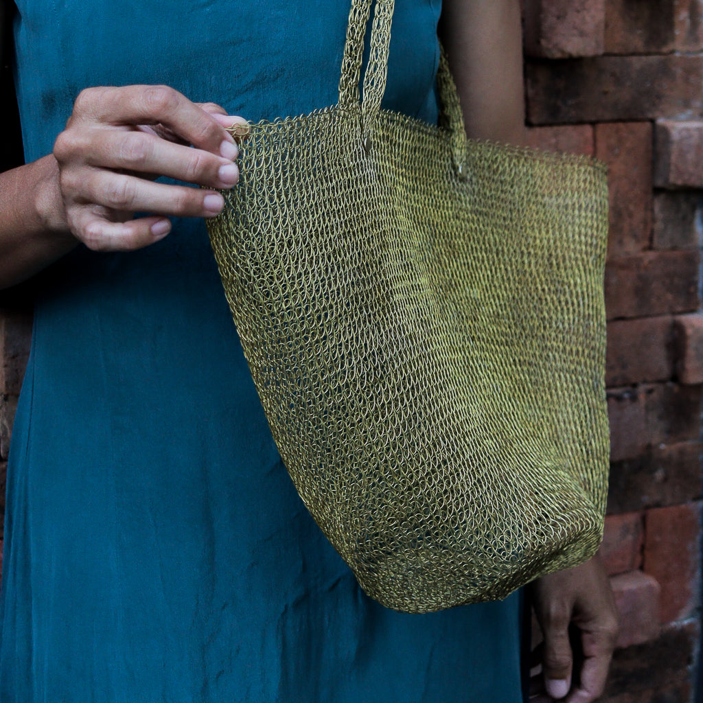 Person holding a green woven bag against a brick wall.