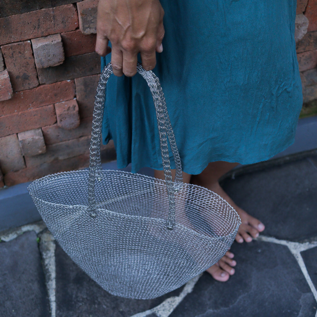 Person holding a silver mesh basket against a brick wall.