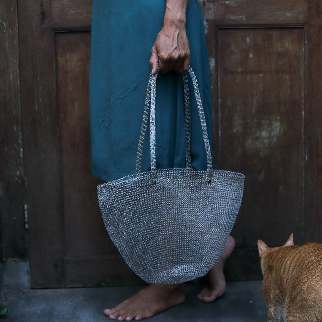 Person holding a textured handbag with a cat in the foreground, wooden door in the background