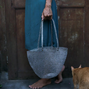 Person holding a textured handbag with a cat in the foreground, wooden door in the background