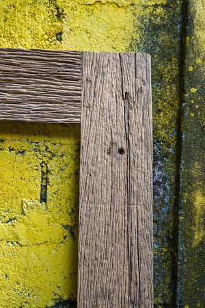 Corner of a rustic wooden frame against a textured yellow wall, handmade home decor