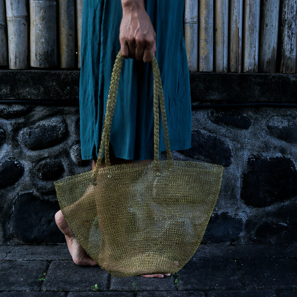 Person holding a woven bag against a stone wall background
