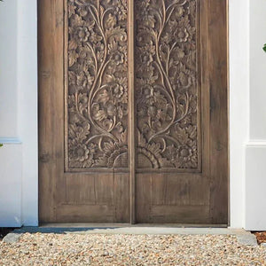 Hand-carved Balinese wooden double door with floral patterns, outdoor setting