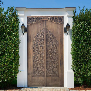 Balinese hand-carved double wooden door with floral patterns in a white outdoor frame
