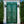 Hand-carved green Balinese door with intricate floral patterns, framed by white pillars and greenery.