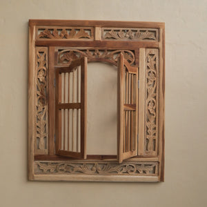 Hand-carved Balinese wooden window frame with intricate floral detailing on a beige wall.