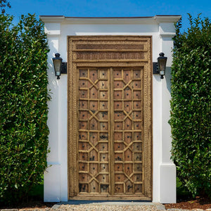 Balinese hand-carved wooden door with intricate patterns in a white outdoor frame