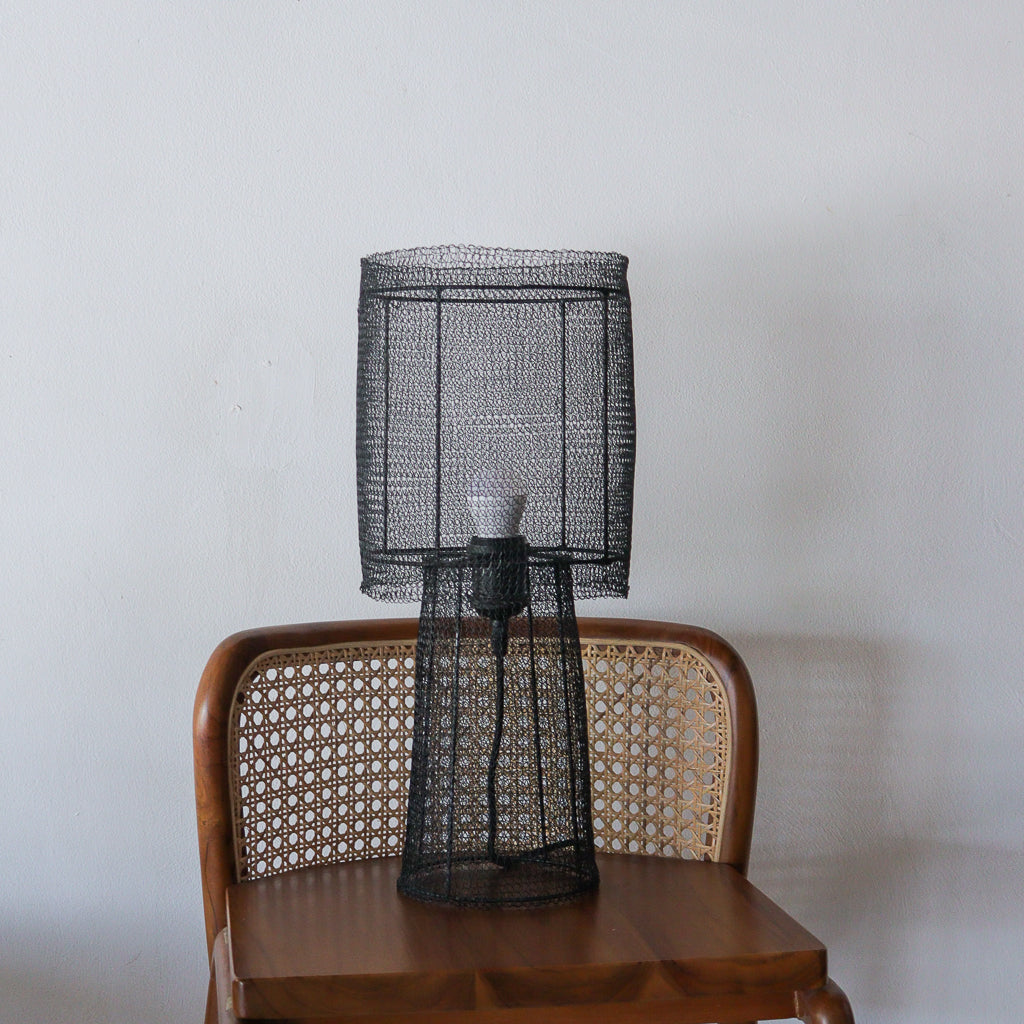 Black wire mesh lamp on a wooden chair against a plain wall