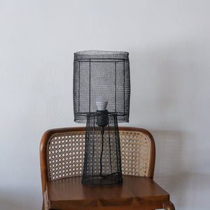 Black wire mesh lamp on a wooden chair against a plain wall