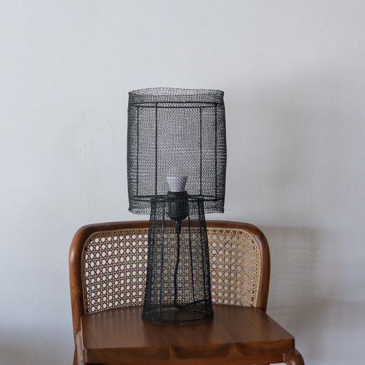 Black wire mesh lamp on a wooden chair against a plain wall