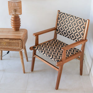 Handwoven rattan chair with geometric pattern beside carved wood table and rattan lamp