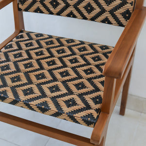 Handwoven rattan chair with geometric black and natural pattern, wooden frame, indoor setting