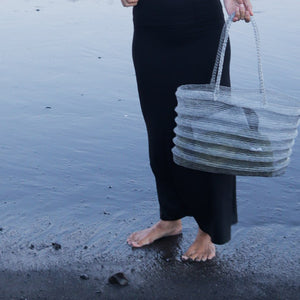 Handwoven seagrass beach bag held by woman on wet sand, eco-friendly coastal accessory