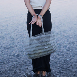 Handwoven beach tote bag held by woman at water’s edge, eco-friendly straw design for summer travel