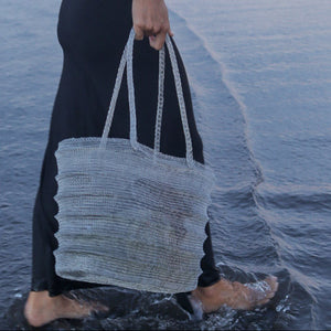 Handwoven seashell tote bag carried by woman walking on beach, eco-friendly beach accessory