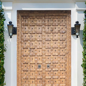 Hand-carved Balinese wooden door with ornate detailing, framed by white walls and lanterns