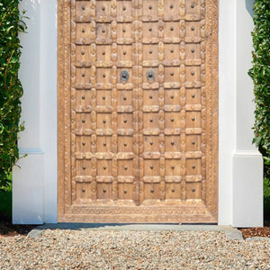 Hand-carved wooden door with intricate Balinese patterns, set in a white exterior frame