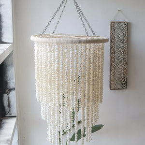 Handcrafted seashell chandelier with cascading beads, hanging in a minimalist room with Balinese wood art.