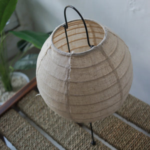 Round linen table lamp with black metal legs on woven rattan surface, natural home decor