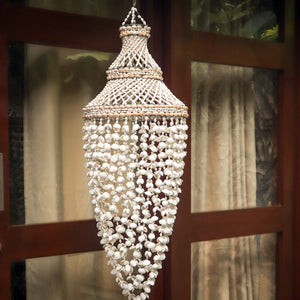 Handmade Balinese seashell chandelier with intricate patterns, hanging indoors by a window