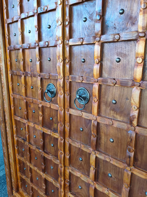 Hand-carved wooden door with geometric patterns and ornate metal ring handles