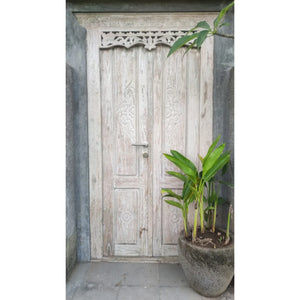 Hand-carved Balinese wooden door with intricate patterns and a potted plant in front