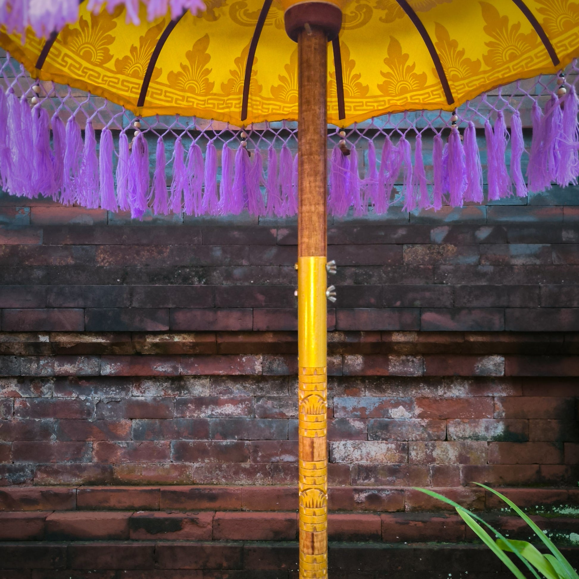 Yellow decorative umbrella with purple tassels against a brick wall