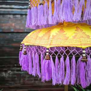 Yellow Balinese decorative parasol with purple fringe tassels and ornate pattern, outdoor decor