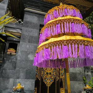 Balinese yellow triple umbrella with purple fringe in front of ornate carved stone gate