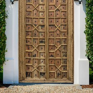 Vintage hand-carved wooden door with geometric patterns set in a white frame outdoors.