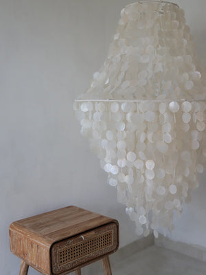 Handmade seashell chandelier and carved wooden side table in minimalist room